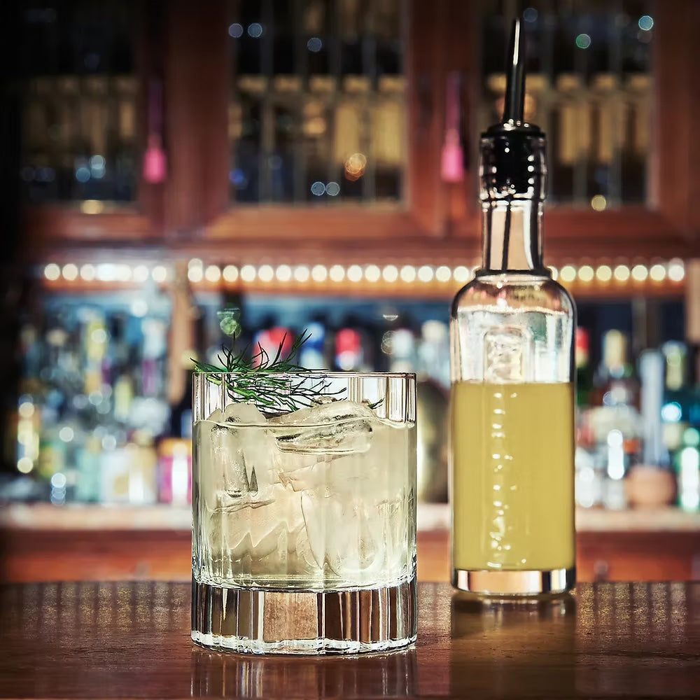 Stylish old fashioned tumbler with drink and ice on bar, textured glass.