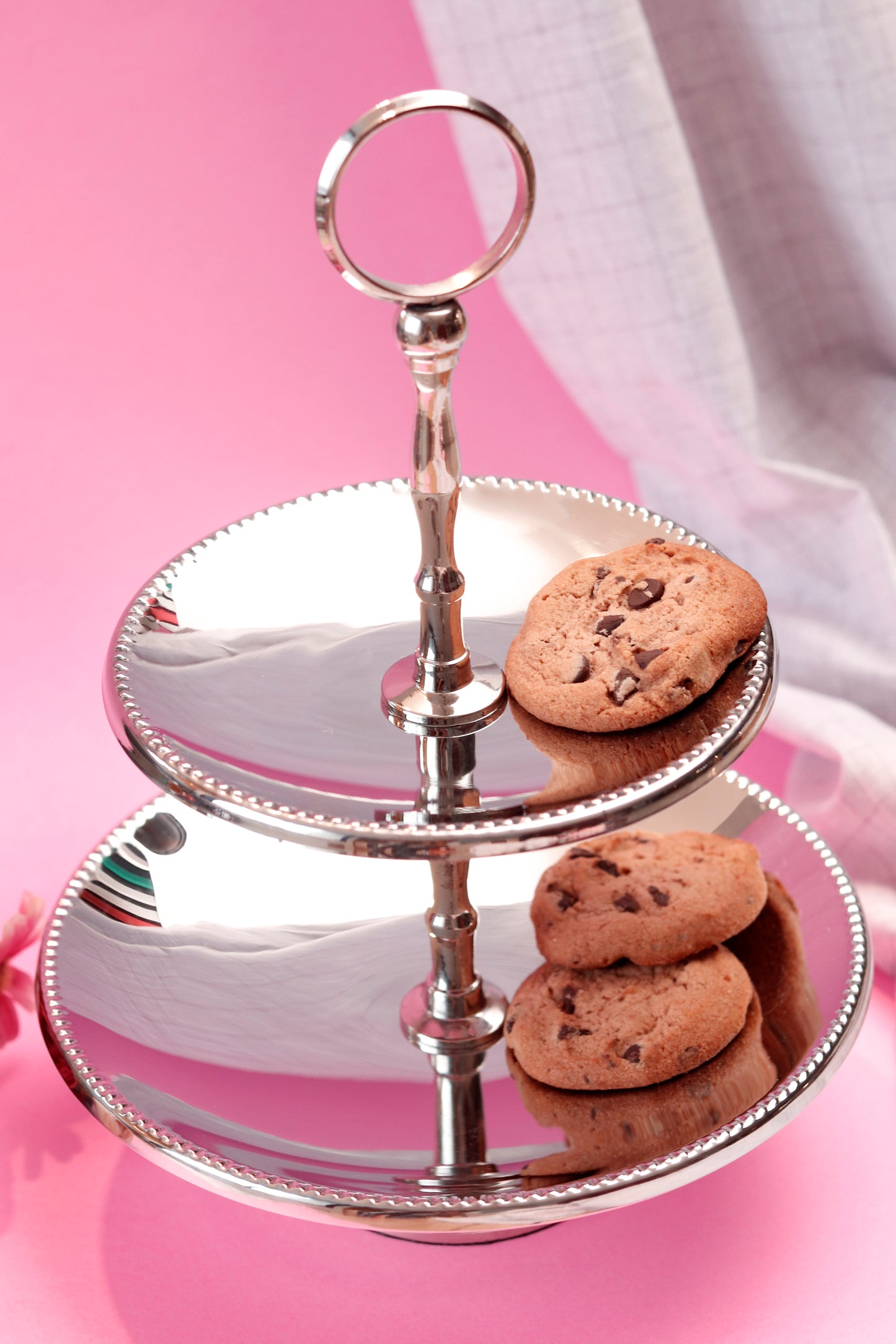 Shiny silver two-tier stand with chocolate chip cookies.