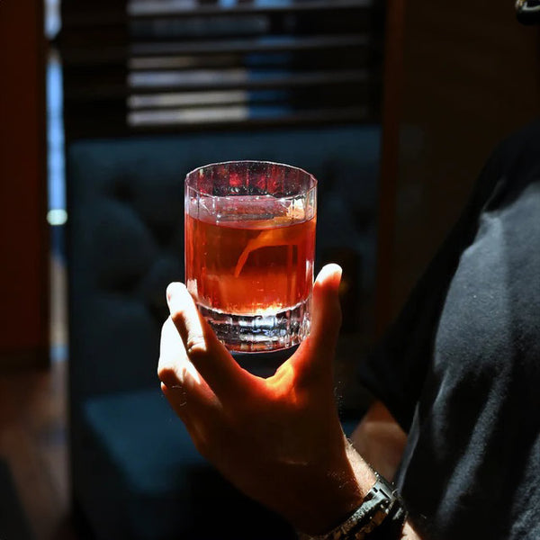 Hand holding old fashioned tumbler with cocktail and orange peel garnish