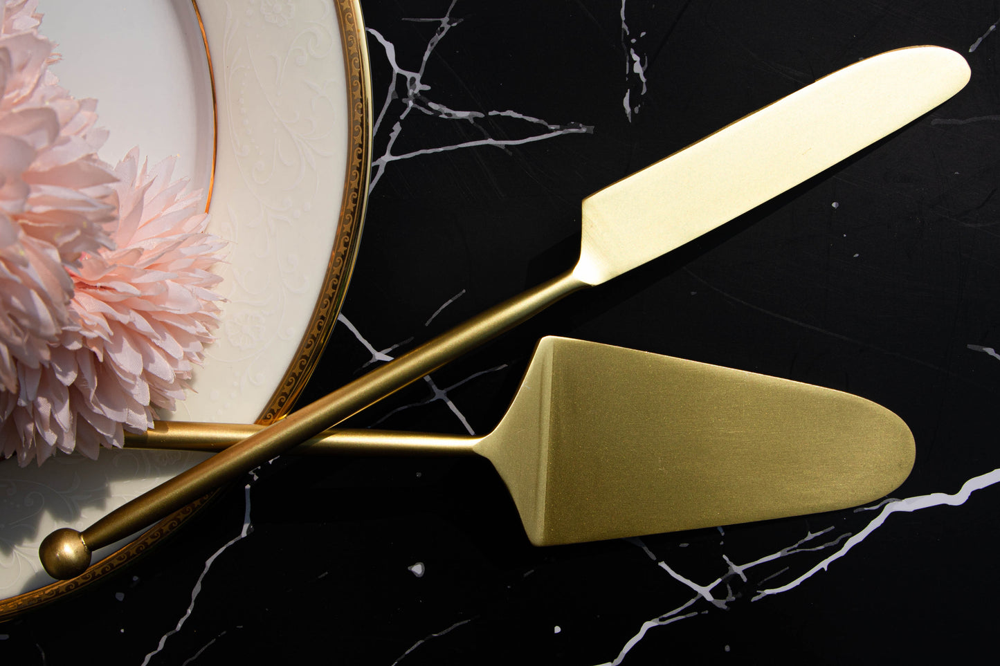 Gold cake server and knife set on a black marble surface.