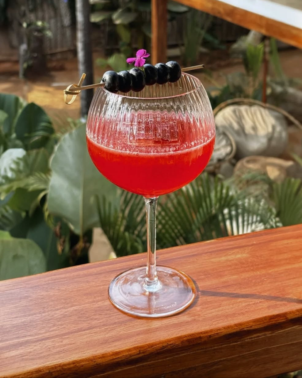 Ribbed cocktail glass filled with red drink and berry garnish.