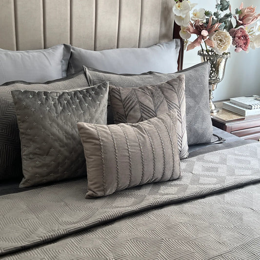Dark grey velvet bedspread with maze pattern and decorative pillows.