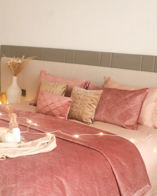 Blush velvet bedspread with quilted pattern and decorative pillows on bed.