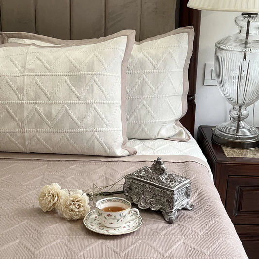 Trigon pattern bedspread with ivory pillows and buff trim.