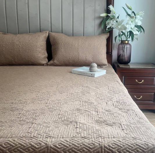 Beige cotton bedspread with quilted pattern and matching pillow shams.