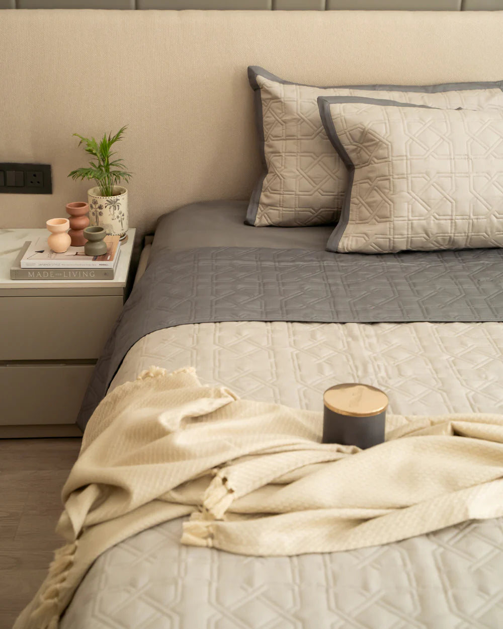 Quilted beige, dark grey reversible bedspread with matching pillows on a made bed.