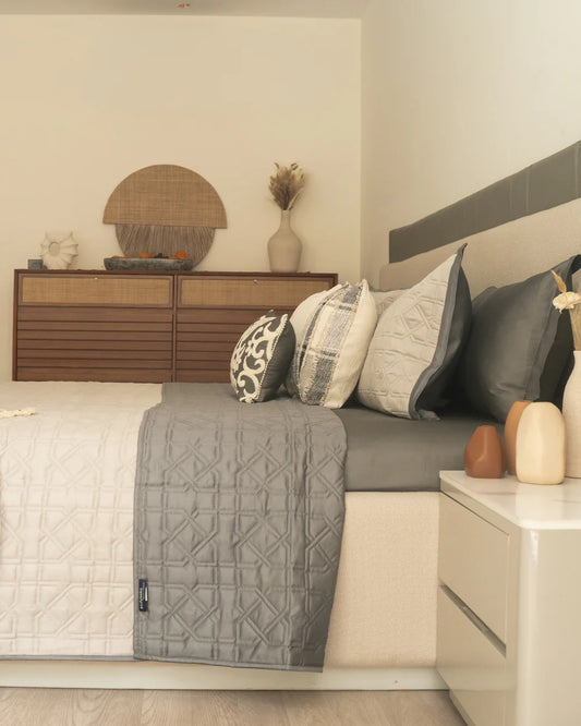Beige and dark grey quilted reversible bedspread on a decorated bed.