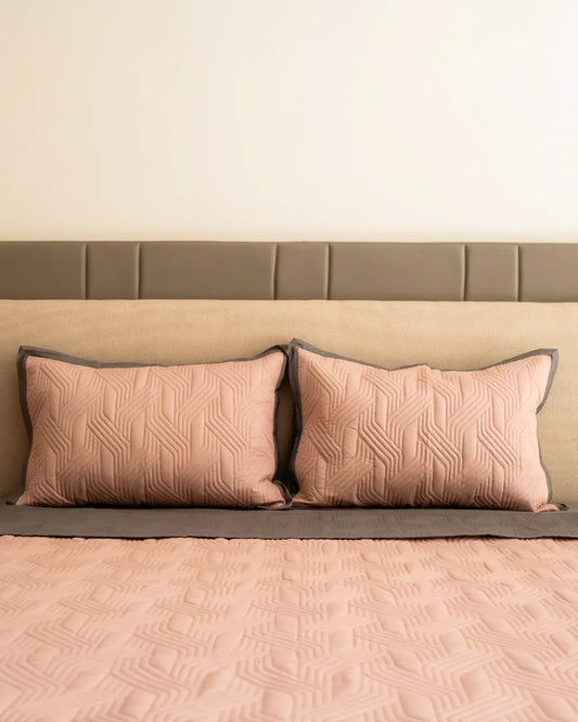 Quilted old rose bedspread with dark grey border and matching pillows.