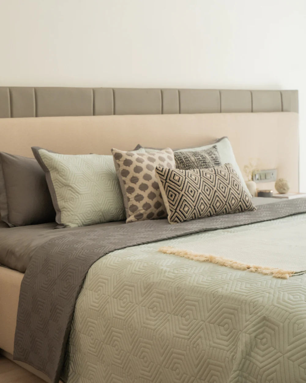 Quilted sage green and dark grey reversible bedspread on a neatly made bed.