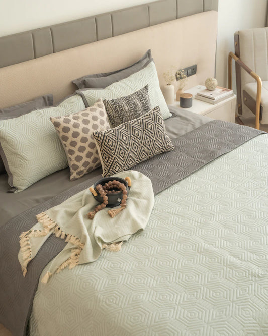 Quilted sage green reversible bedspread with dark grey accent, decorative pillows.
