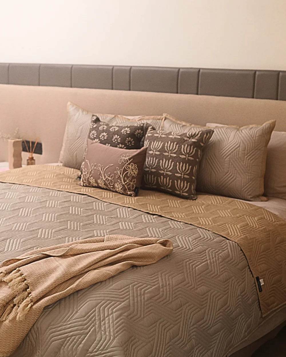 Sand beige quilted bedspread with decorative pillows and cozy throw blanket.