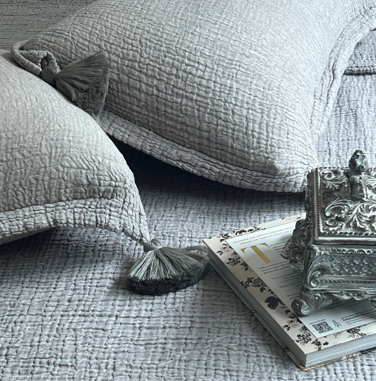 Slate woven bedspread with textured pattern and tasseled pillows.