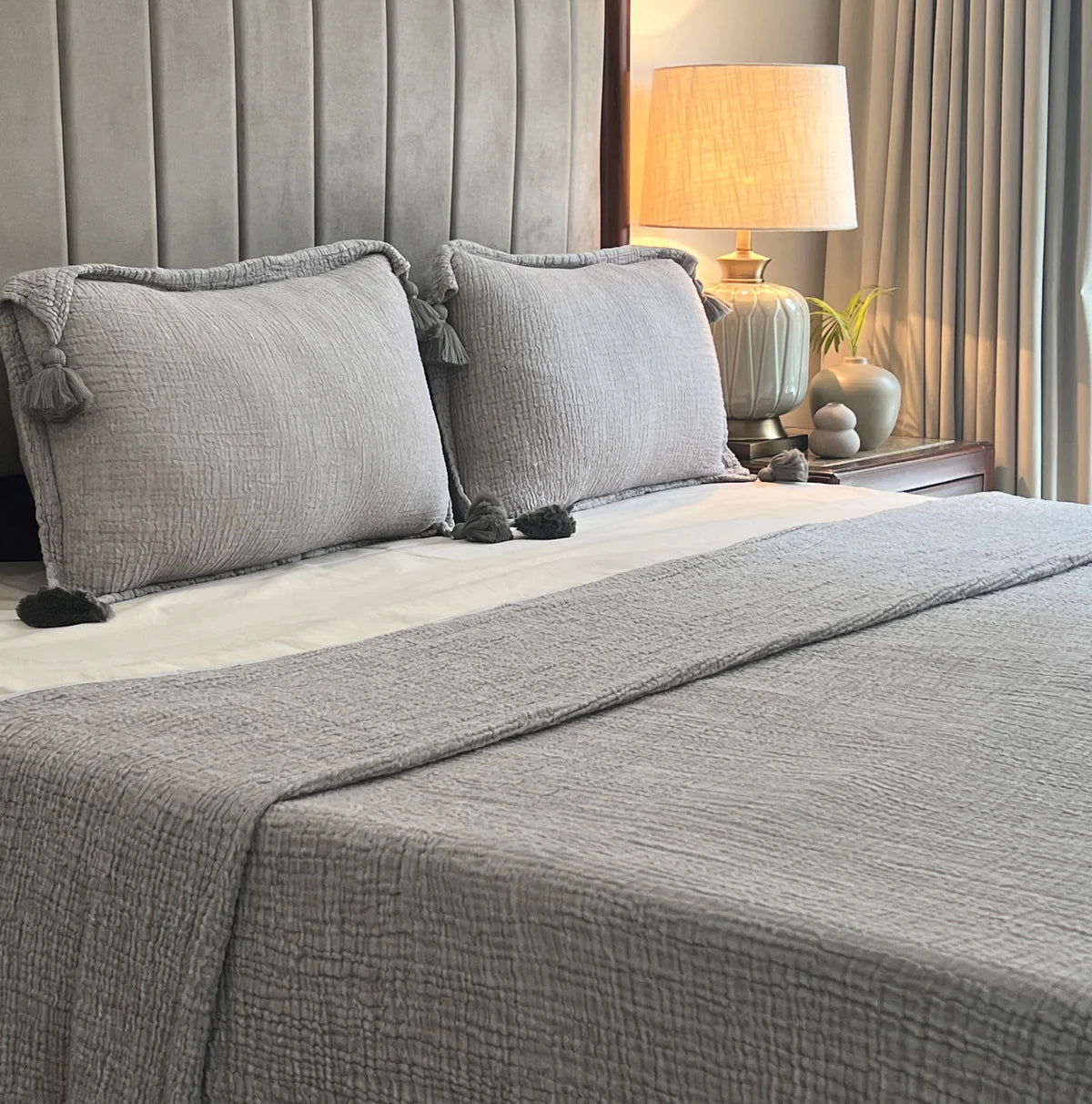 Slate woven bedspread with textured pattern and tassel cushion details.