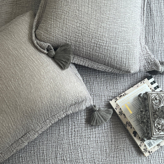 Slate woven bedspread with textured pillows and tassel details.
