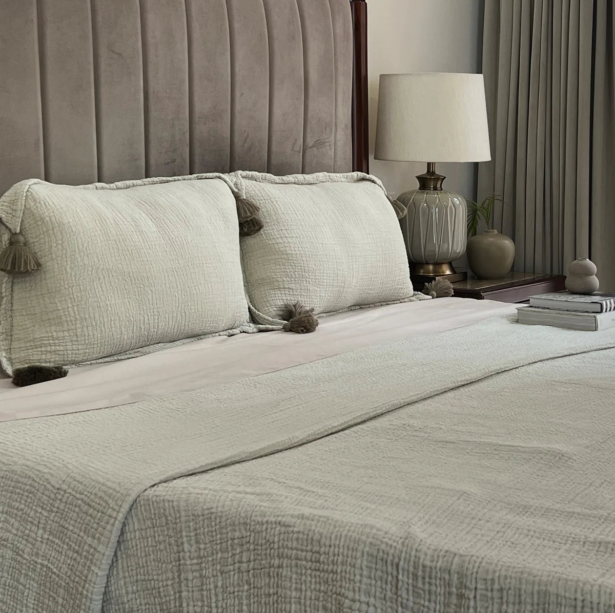 Sage woven bedspread with tassel pillow on a made bed.