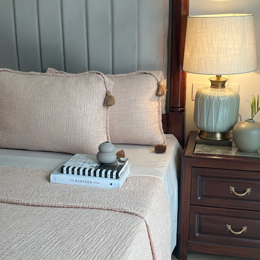 Sage woven bedspread with tassel pillows on a made bed.