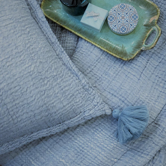 Indigo woven bedspread with a textured pillow and tassel.