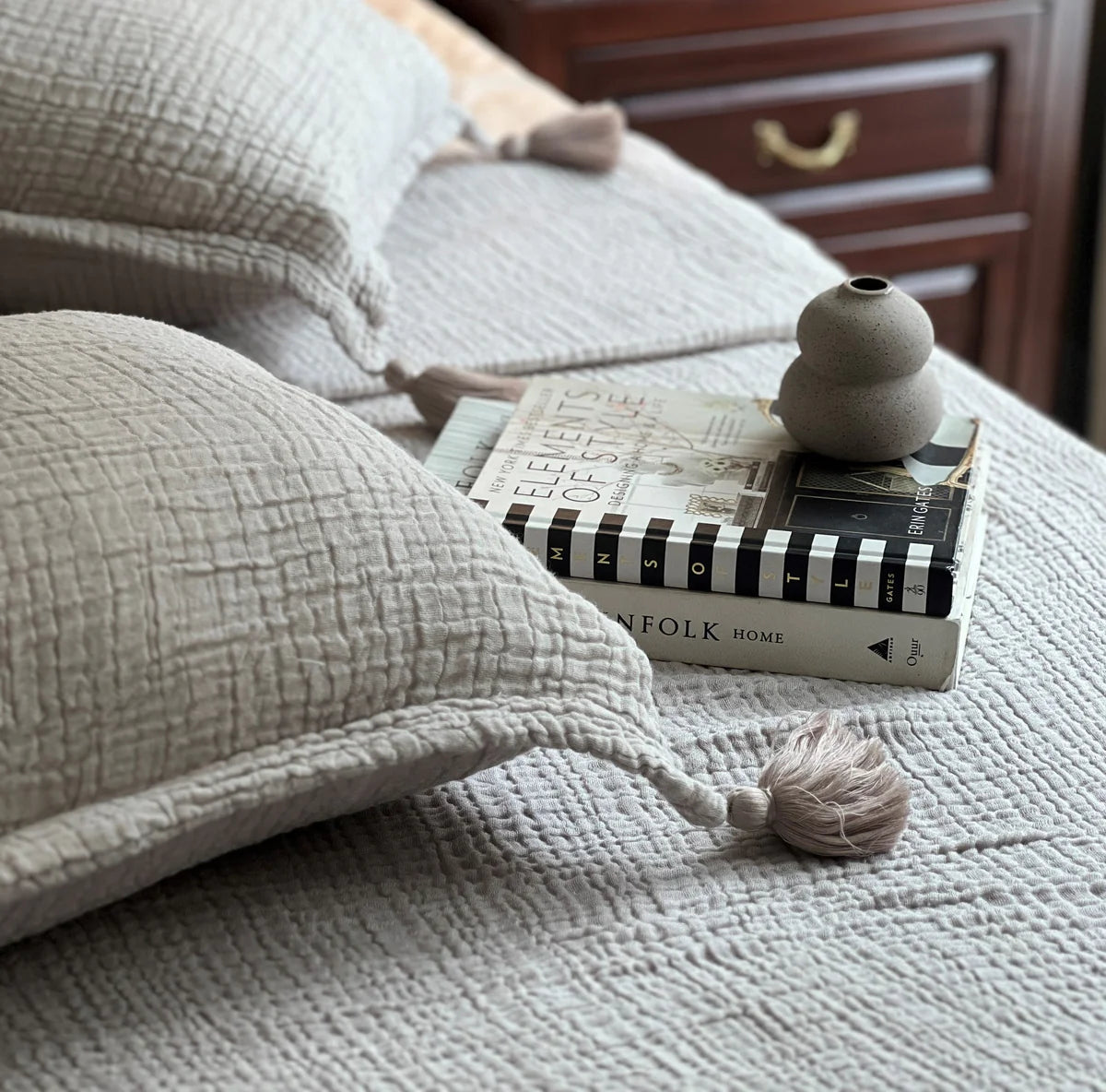Greige woven bedspread with textured design and tassels on a neatly made bed.
