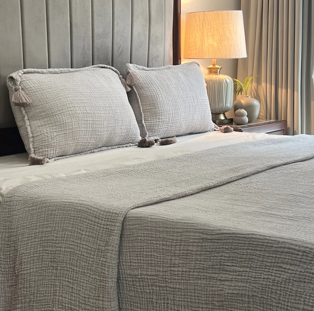 Greige woven bedspread with textured pattern and matching tassel pillow shams.
