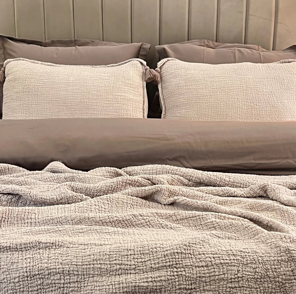 Buff woven bedspread with textured design and decorative tassel pillows.