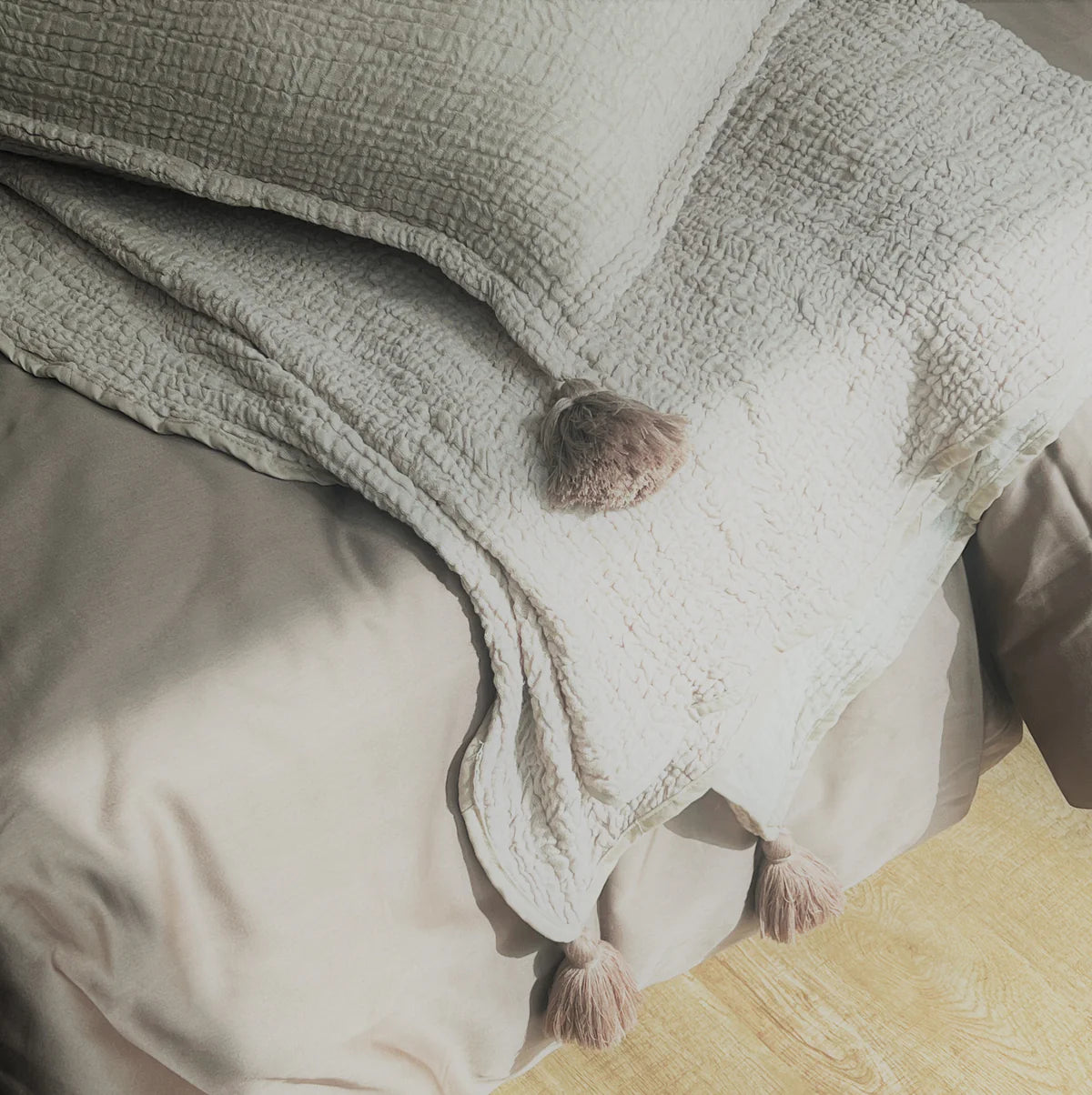 Buff woven bedspread with tassels on a neatly made bed.