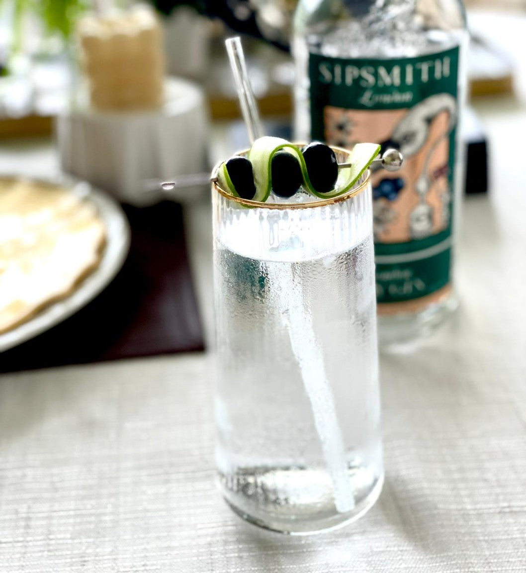 Elegant highball glass with gold rim and olive garnish.