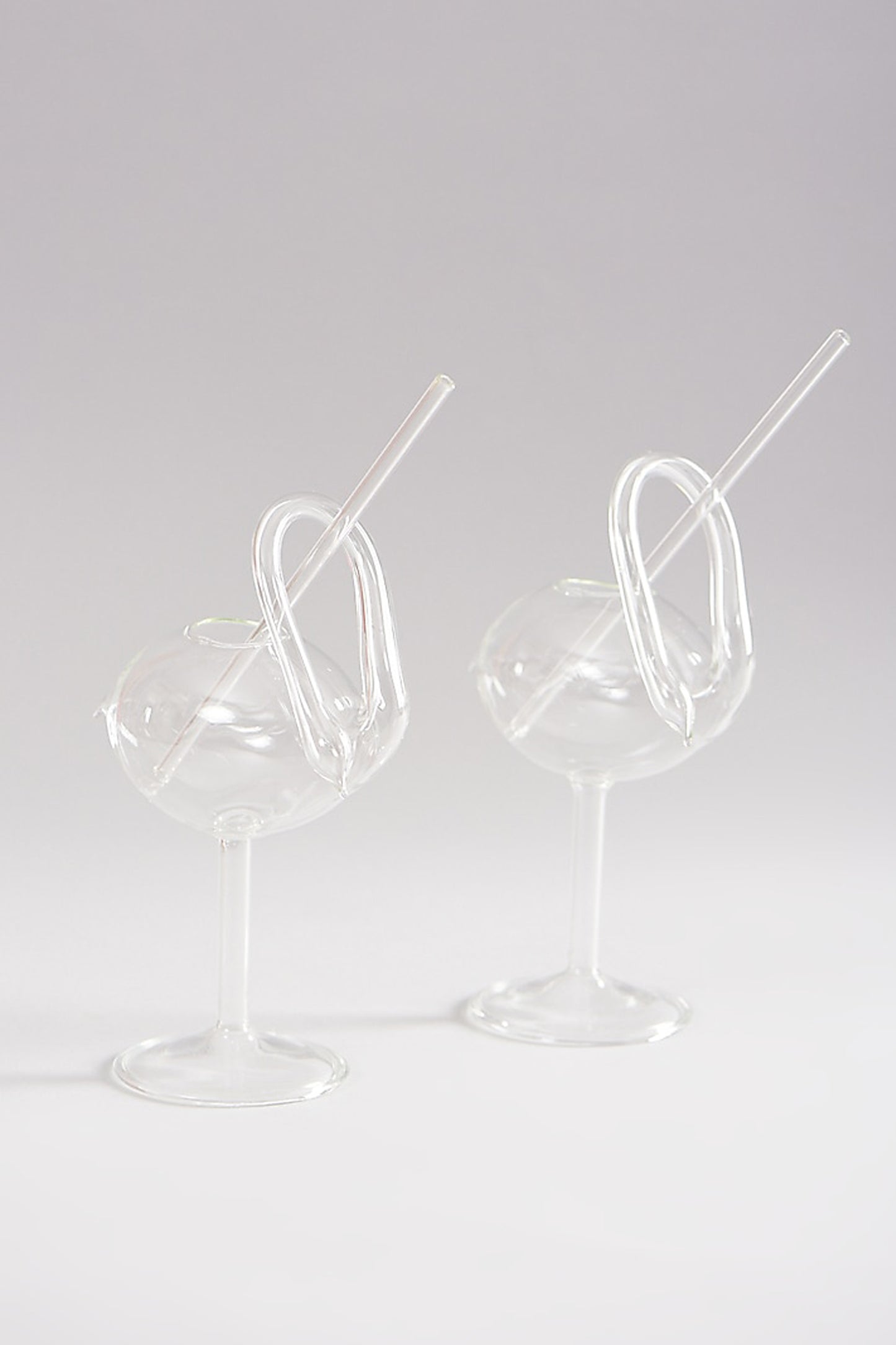 Two swan shaped clear cocktail glasses with straws.