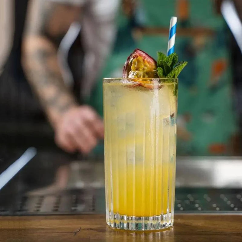 Refreshing drink in ribbed highball glass with fruit garnish and striped straw.