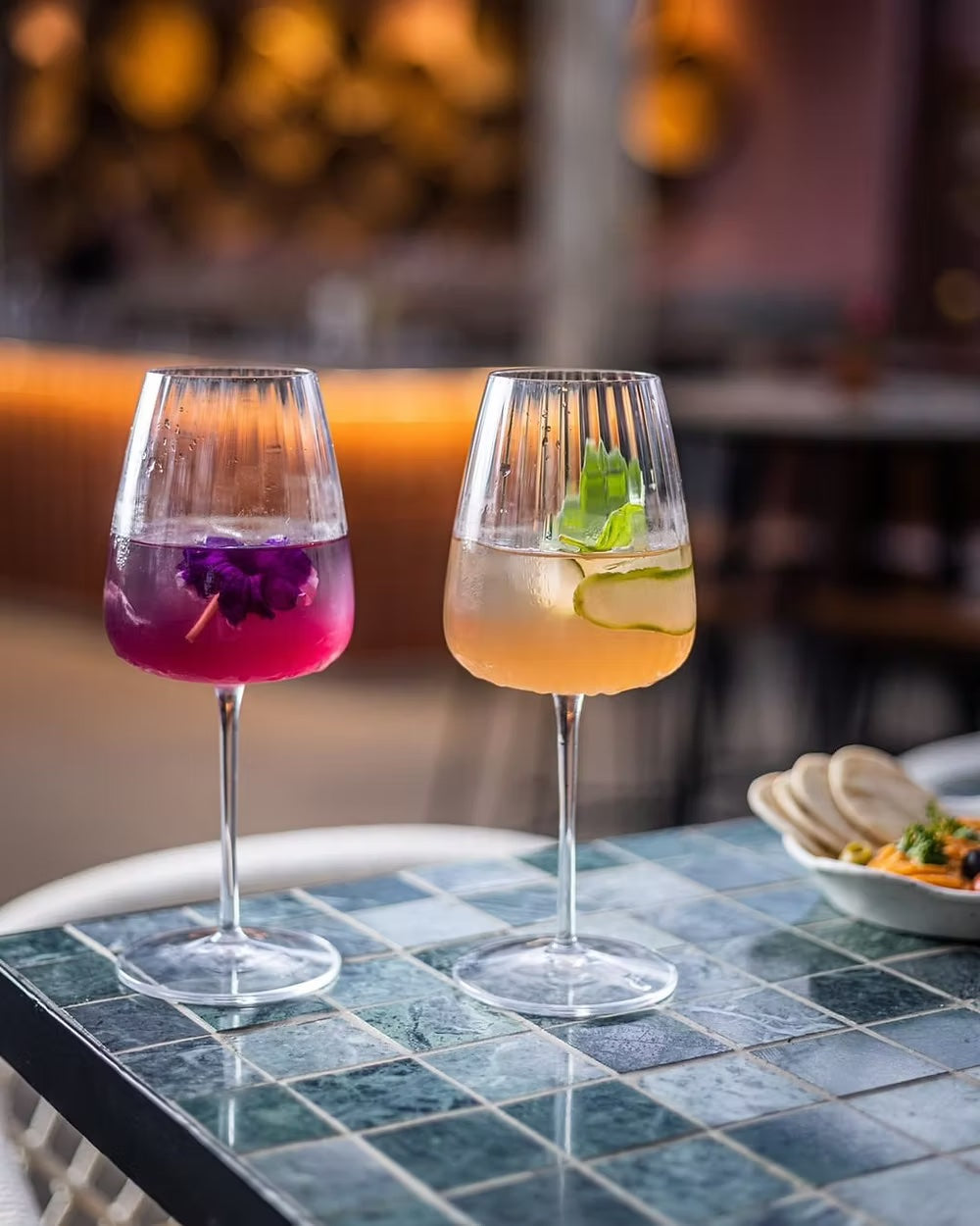 Optica fluted white wine glasses with colorful drinks and fresh garnish.