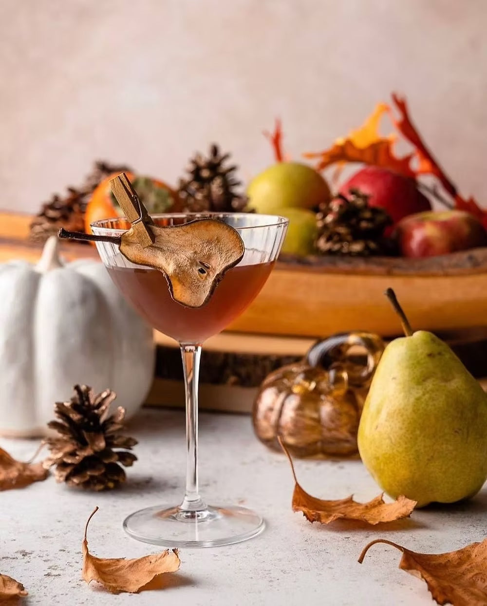 Optica martini glass filled with cocktail and pear garnish with fall decorations.