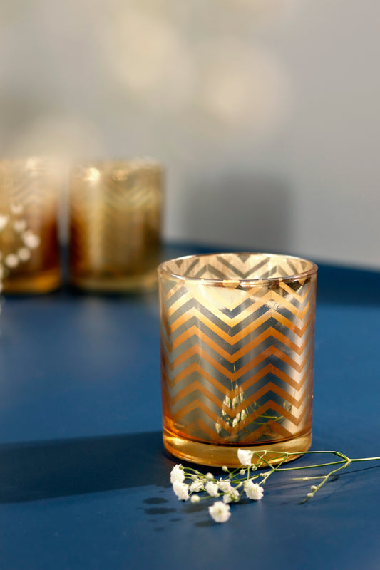 Gold chevron candle set on a blue surface with floral accent.