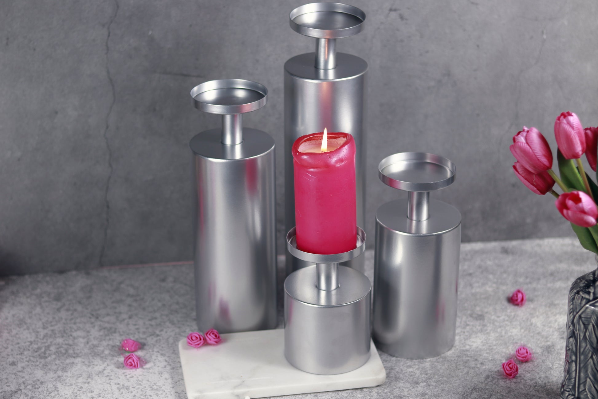 Chrome candle stands of varying heights with a lit candle.