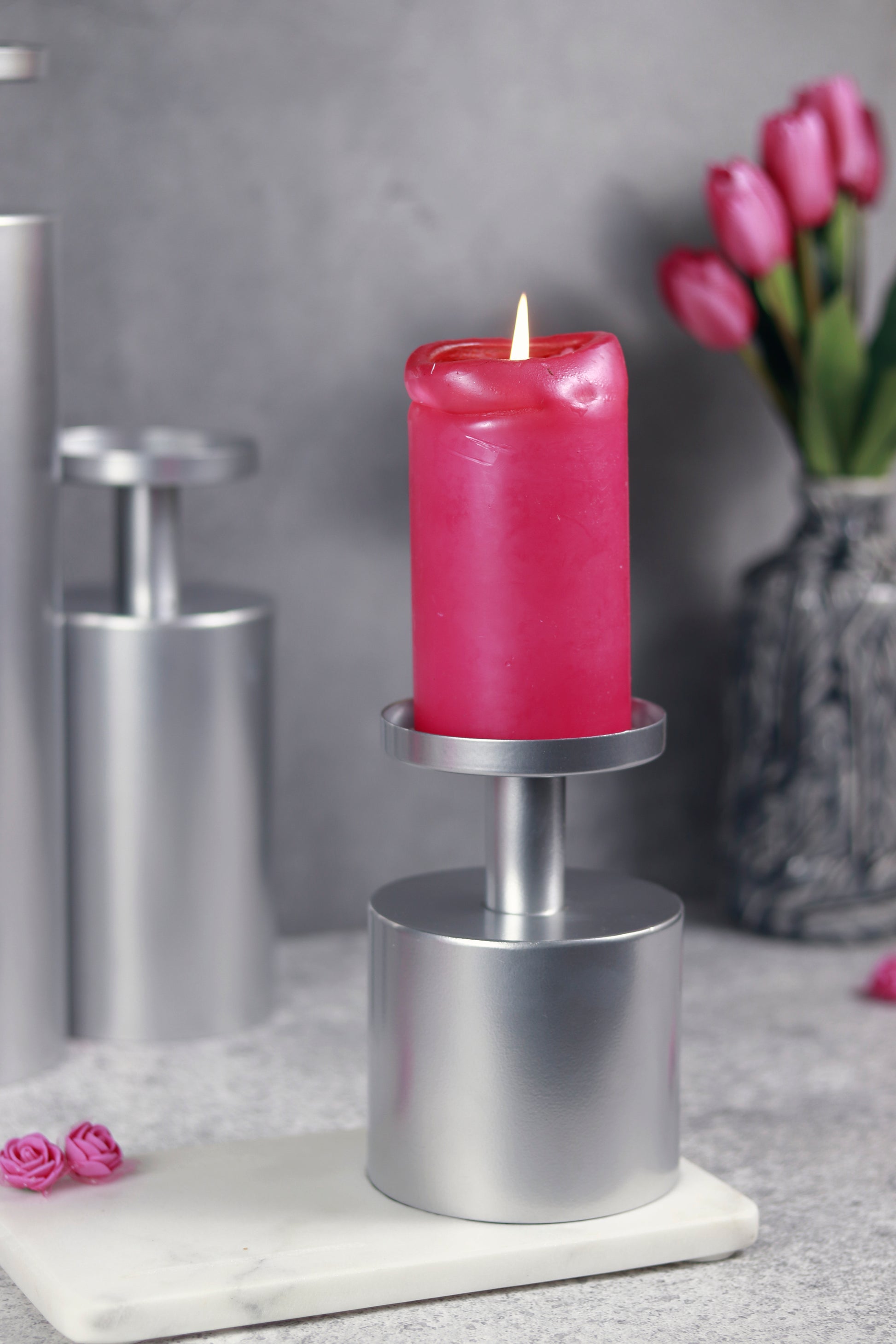 Lit pink candle atop a modern chrome candle stand, decorative.