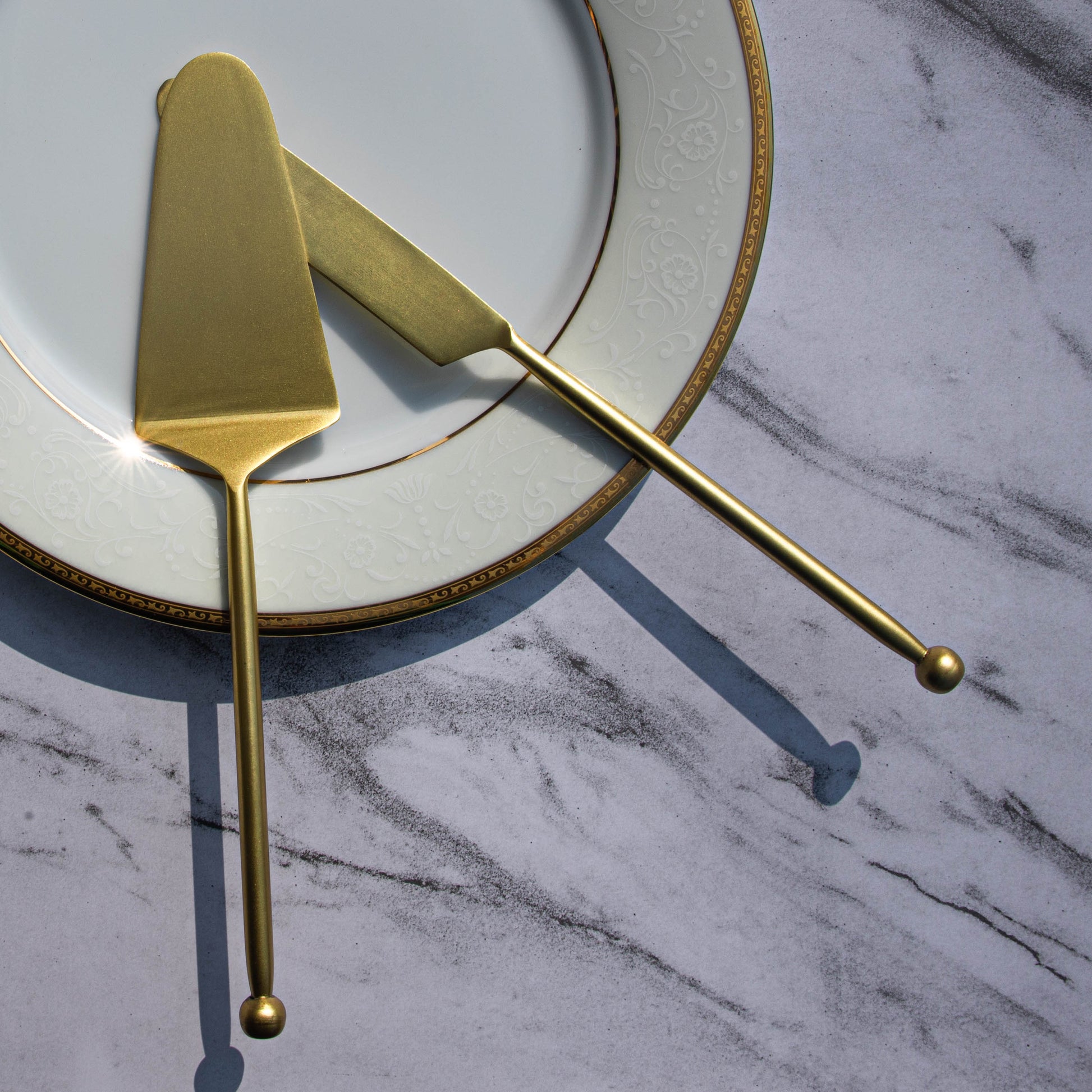 Elegant gold cake knife and server on a decorative plate.