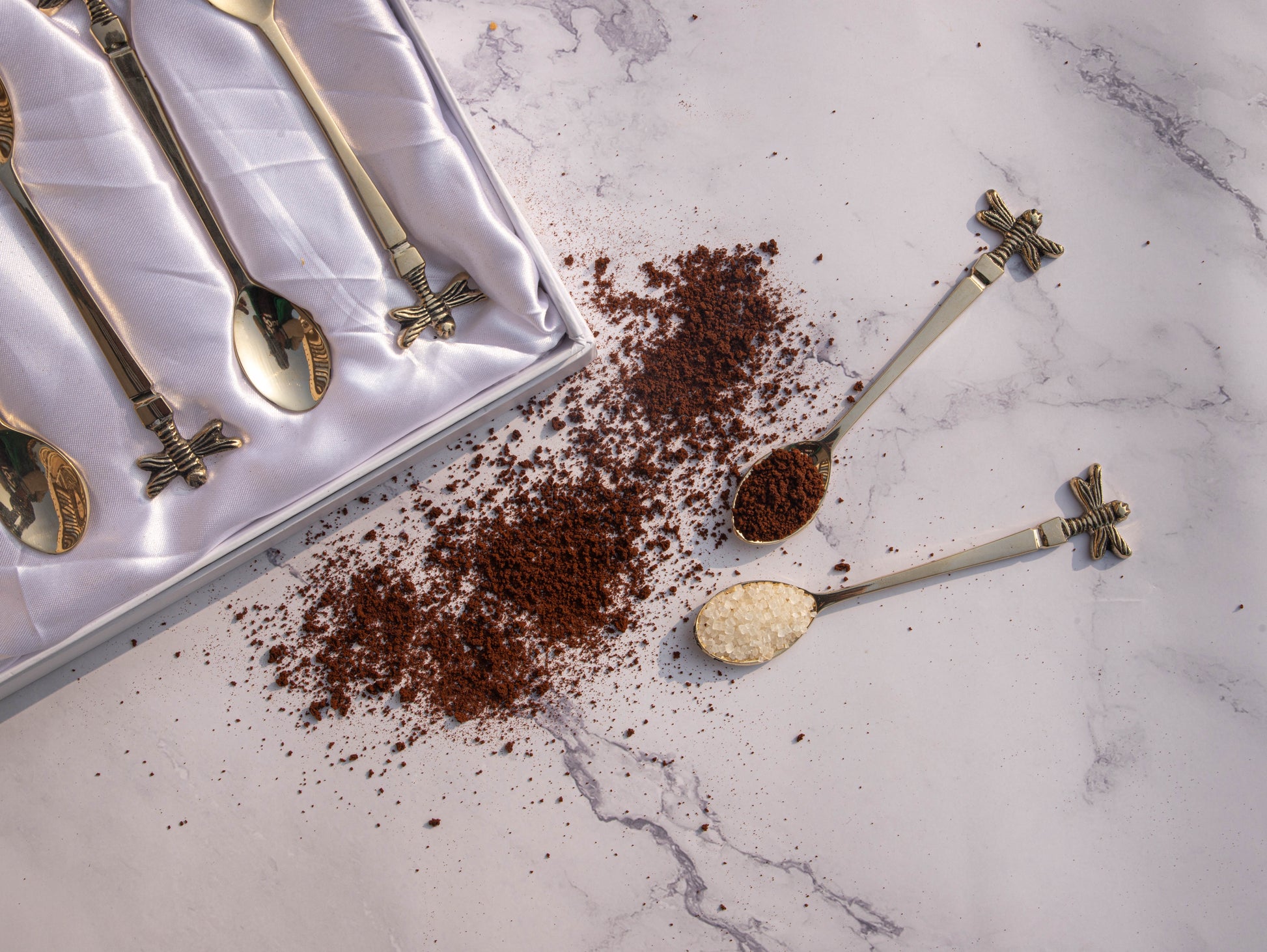 Elegant tea spoons with dragonfly design and coffee grounds.