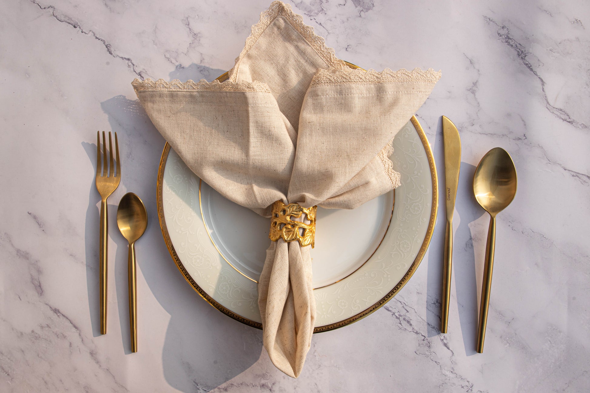 Ornate leaf napkin ring on plate with linen napkin and golden cutlery.