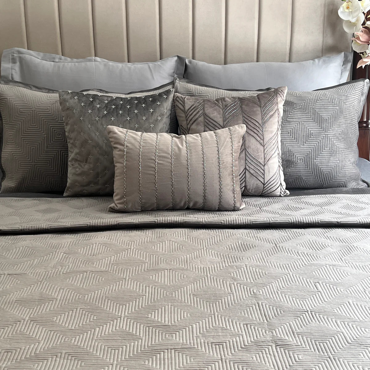 Dark grey velvet bedspread with a maze pattern and decorative pillows.