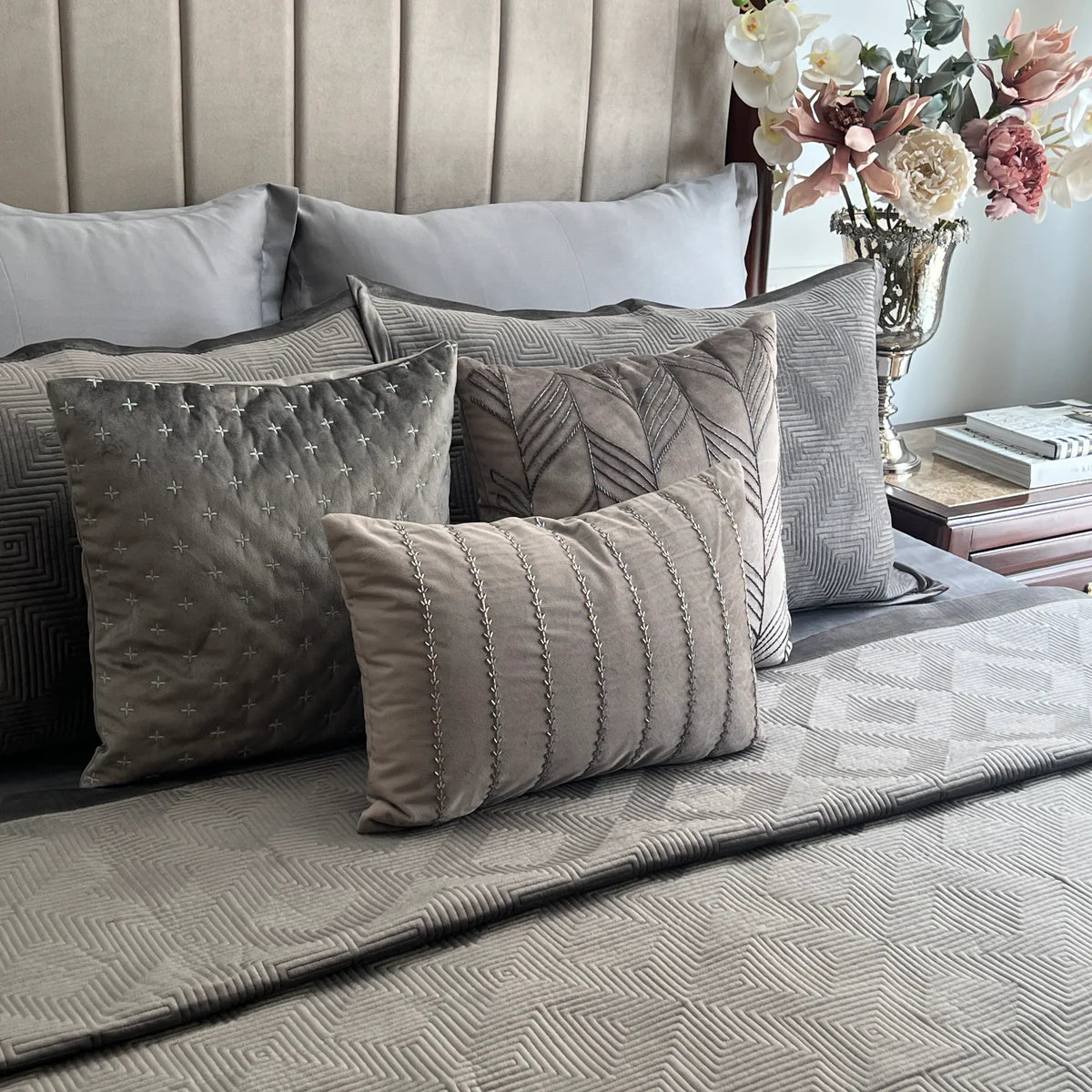 Dark grey velvet bedspread with maze pattern and decorative pillows.