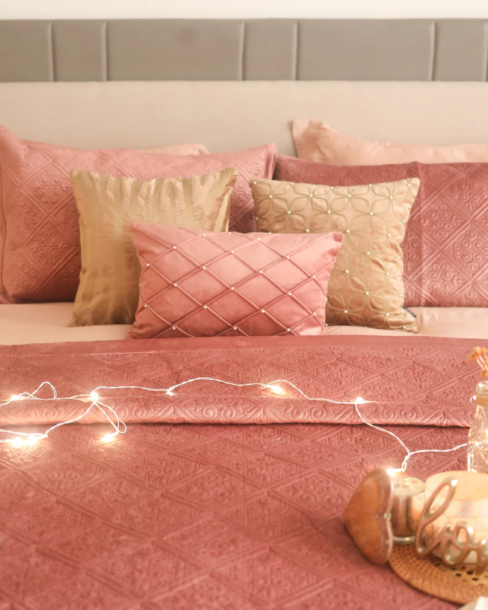 Blush velvet bedspread with quilted pattern and decorative pillows.