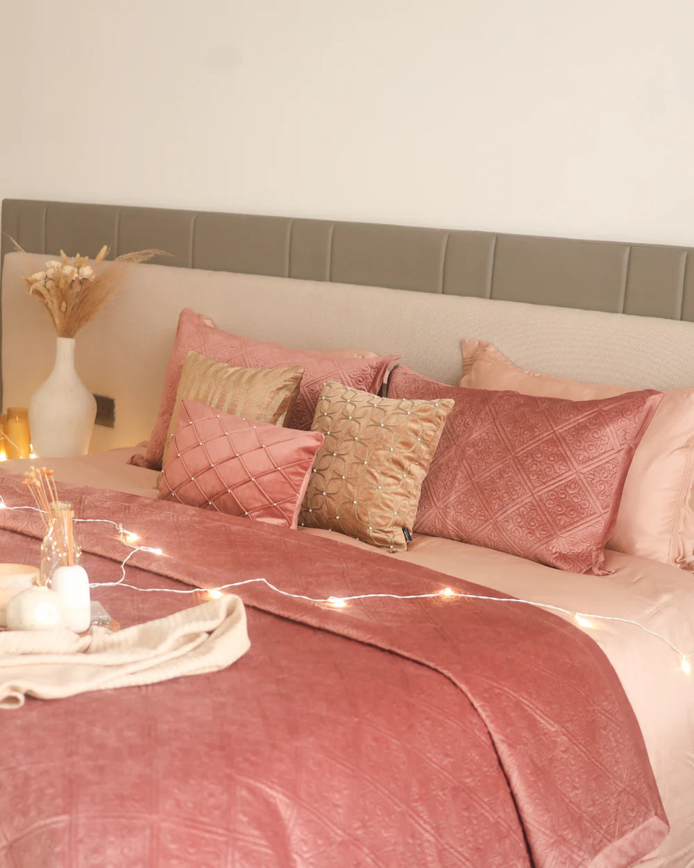 Blush velvet bedspread with quilted pattern and decorative pillows on bed.