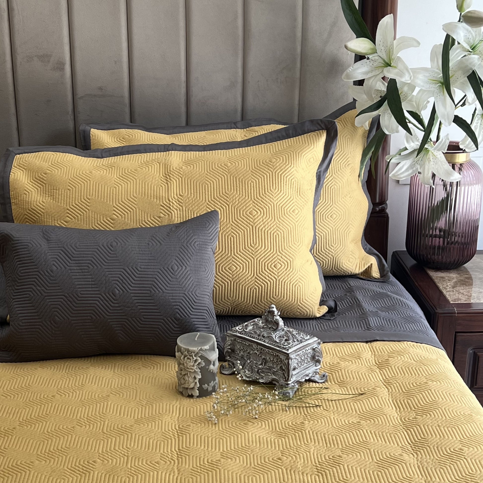Buttercup yellow bedspread with geometric pattern and dark grey cotton pillows.