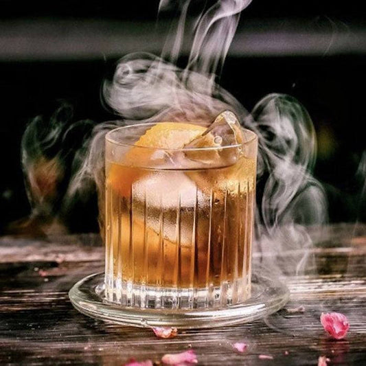 DOF Tumbler with drink, ice, and lemon. Glassware sits on a glass coaster with vapor.