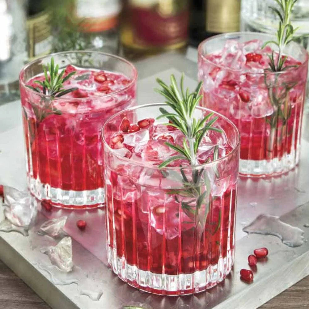 Set of six clear, fluted DOF tumblers with pomegranate cocktail and rosemary.